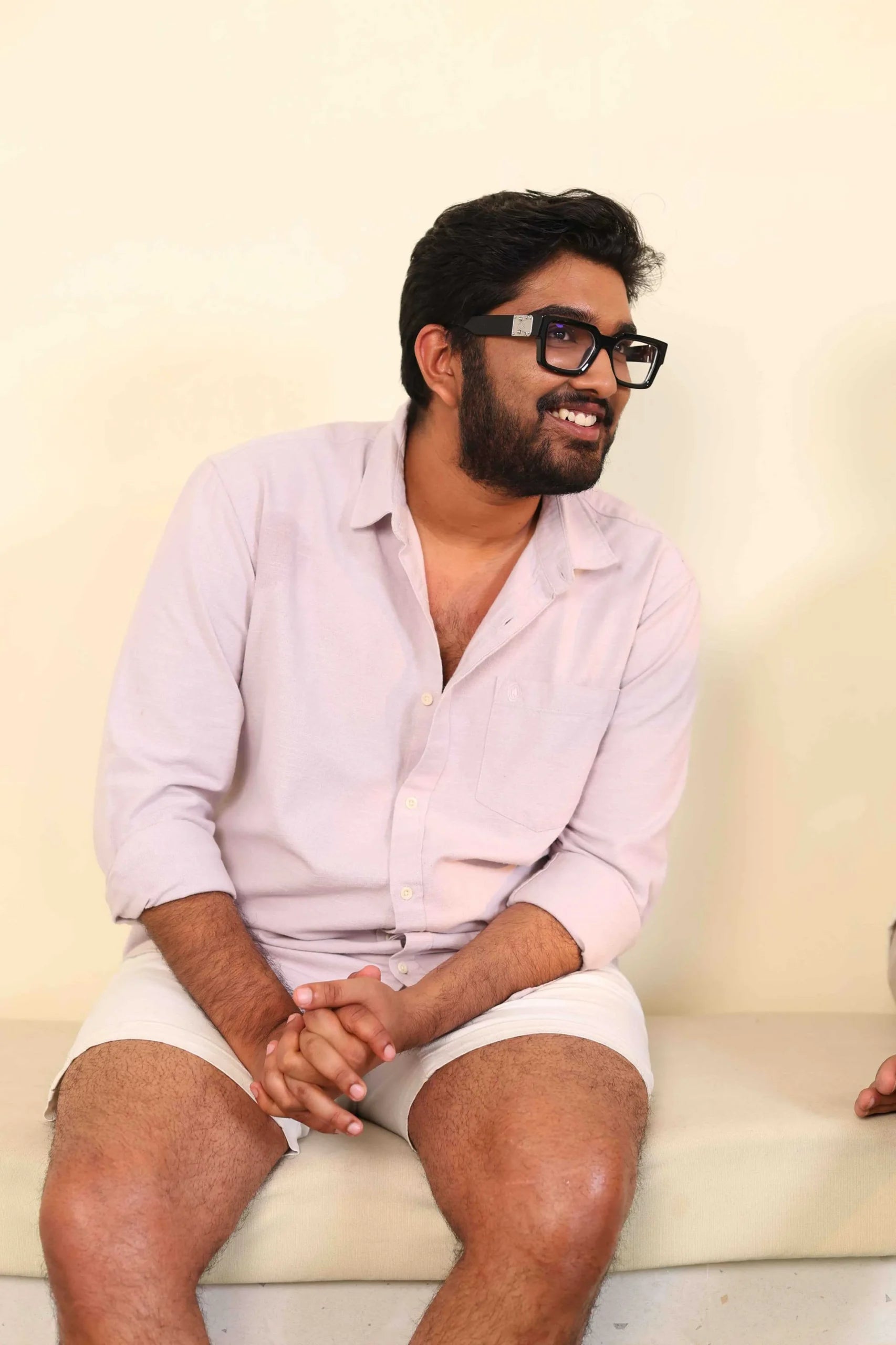 Man in light pink shirt smiling, seated with hands behind him.