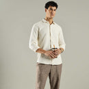 Man wearing a white shirt and brown pants holding a drink against a gray background