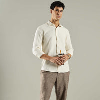 Man wearing a white shirt and brown pants holding a drink against a gray background