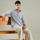 Man sitting on a wooden bench wearing a light blue shirt and beige pants.