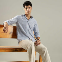 Man sitting on a wooden bench wearing a light blue shirt and beige pants.