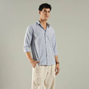 Man wearing a light blue striped shirt and beige pants against a gray background