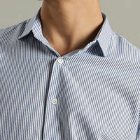 Close-up of a person wearing a blue and white striped shirt against a neutral background