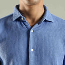 Close-up of a person wearing a blue textured shirt with a neutral background