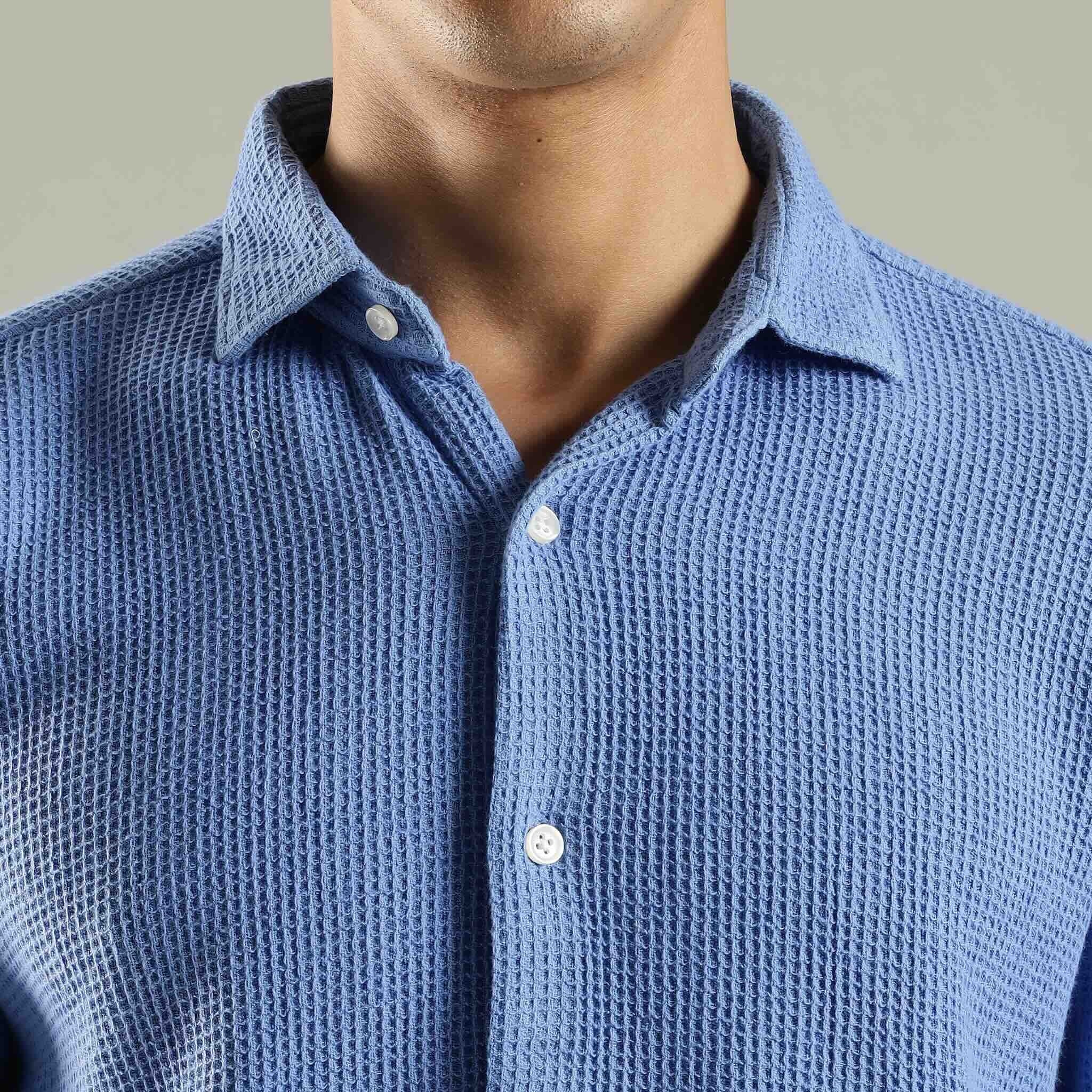 Close-up of a person wearing a blue textured shirt with a neutral background