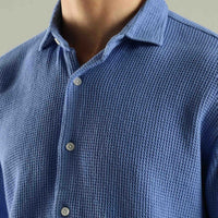 Close-up of a blue textured shirt with buttons on a neutral background