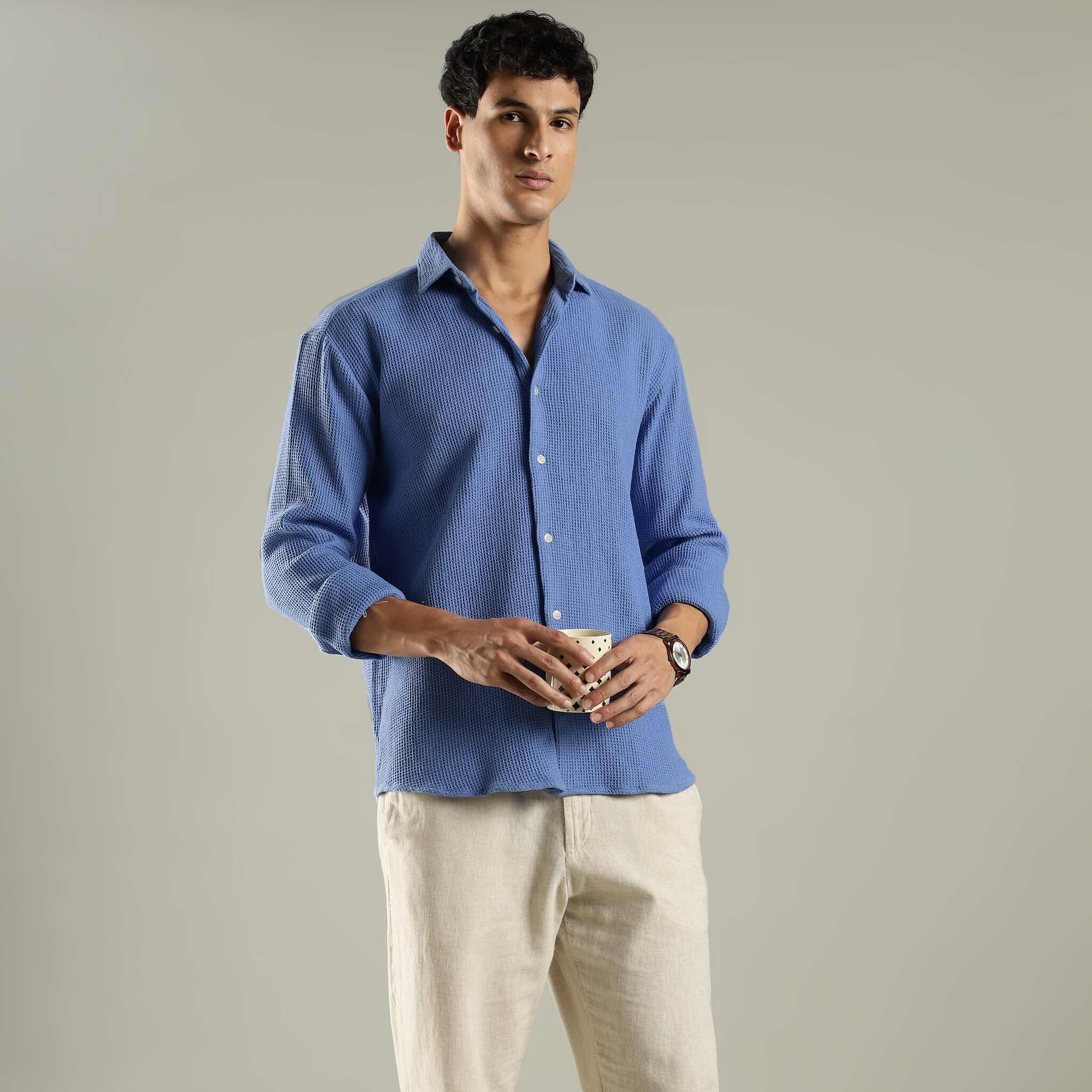 Man wearing a blue textured shirt and beige pants against a plain background