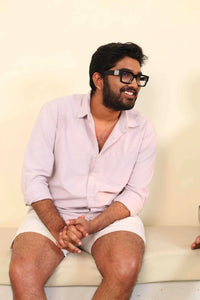 Man in light pink shirt smiling, seated with hands behind him.