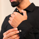 Person adjusting the cuff of a black shirt against a neutral background