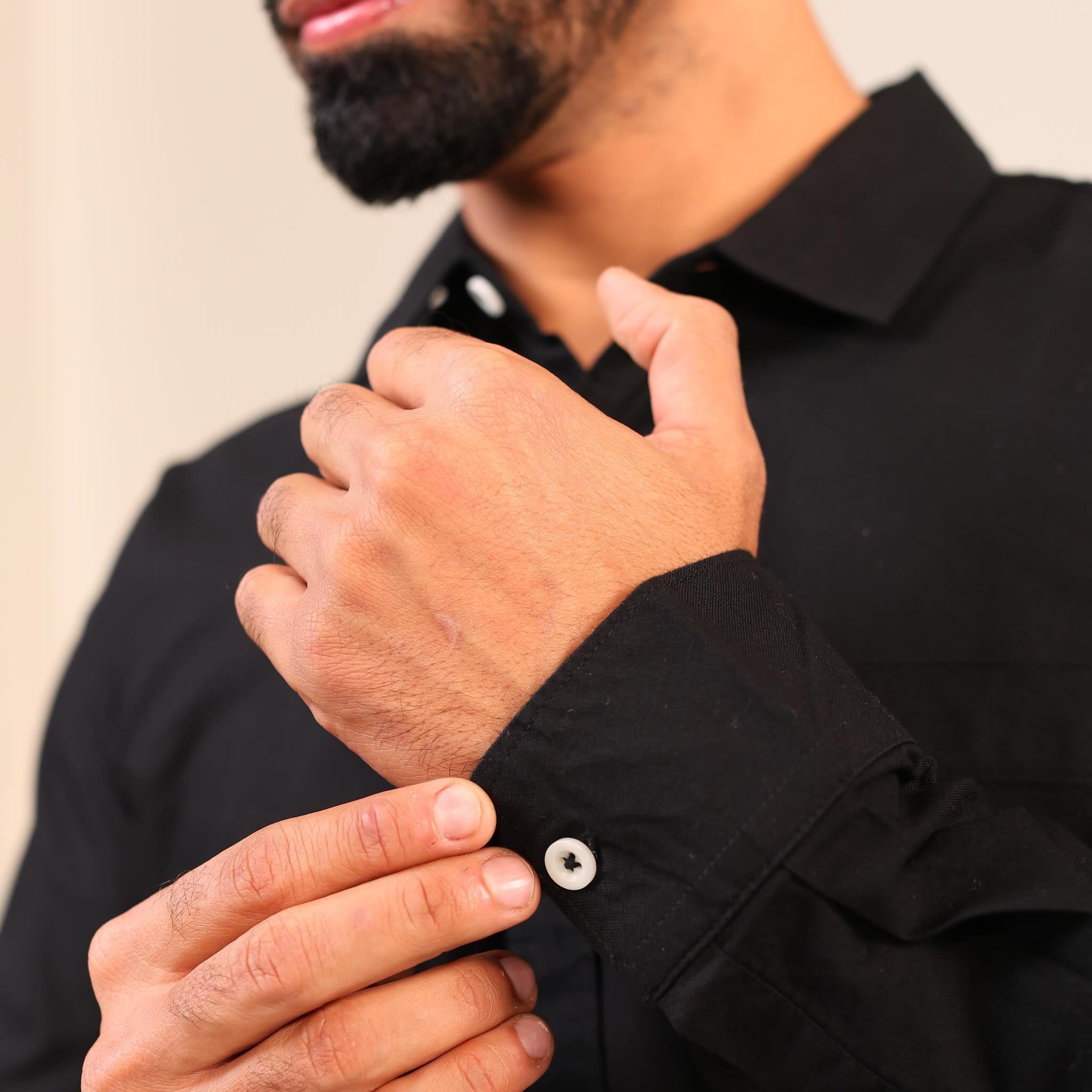 Person adjusting the cuff of a black shirt against a neutral background