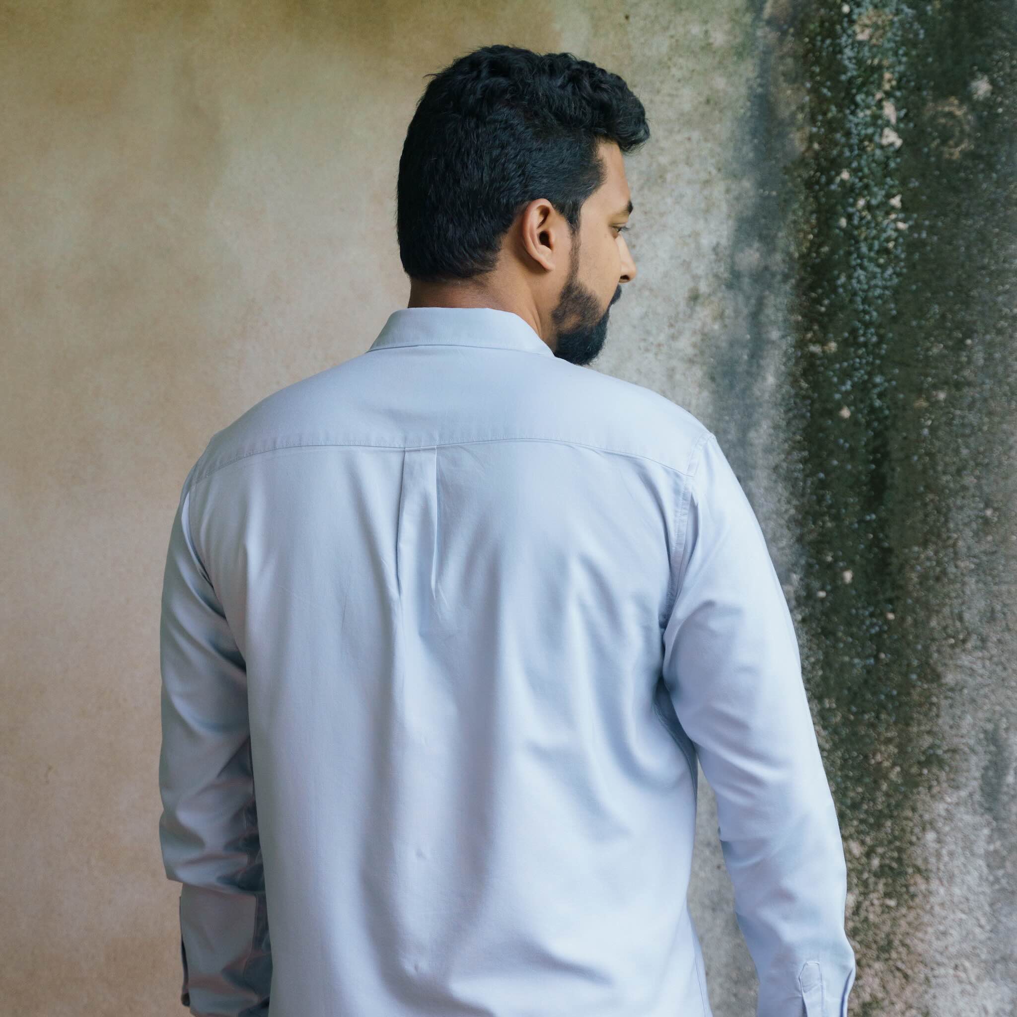 Man wearing a light blue shirt against a textured wall.