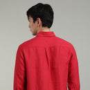 Man wearing a red linen shirt facing against a gray background