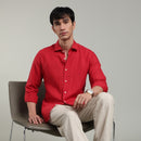 Man wearing a red linen shirt sitting on a chair against a gray background