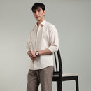 Man wearing a beige shirt and brown pants leaning against chair  