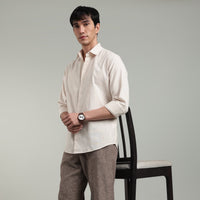 Man wearing a beige shirt and brown pants leaning against chair  