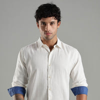 Man wearing a white shirt with blue cuffs against a gray background