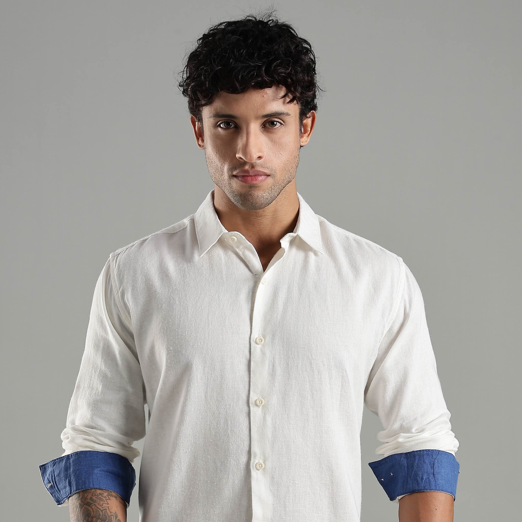 Man wearing a white shirt with blue cuffs against a gray background