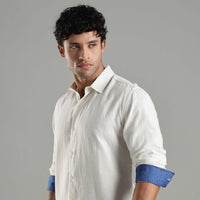 Man wearing a white shirt with blue cuffs against a gray background