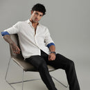 Man sitting on a chair wearing a white shirt with rolled-up sleeves and black pants against a gray background