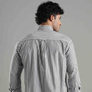 Man wearing a striped shirt and sunglasses facing backwards against a gray background