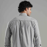 Man wearing a striped shirt and sunglasses facing backwards against a gray background