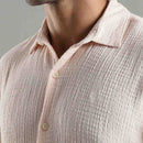 Close-up of a person wearing a textured light pink shirt with a neutral background