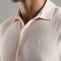 Close-up of a person wearing a textured light pink shirt with a neutral background