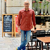Man in a red shirt standing in an outdoor setting with tables and a chalkboard sign.