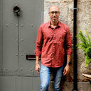 Man wearing a red shirt and blue jeans standing in front of a textured wall and metal door.
