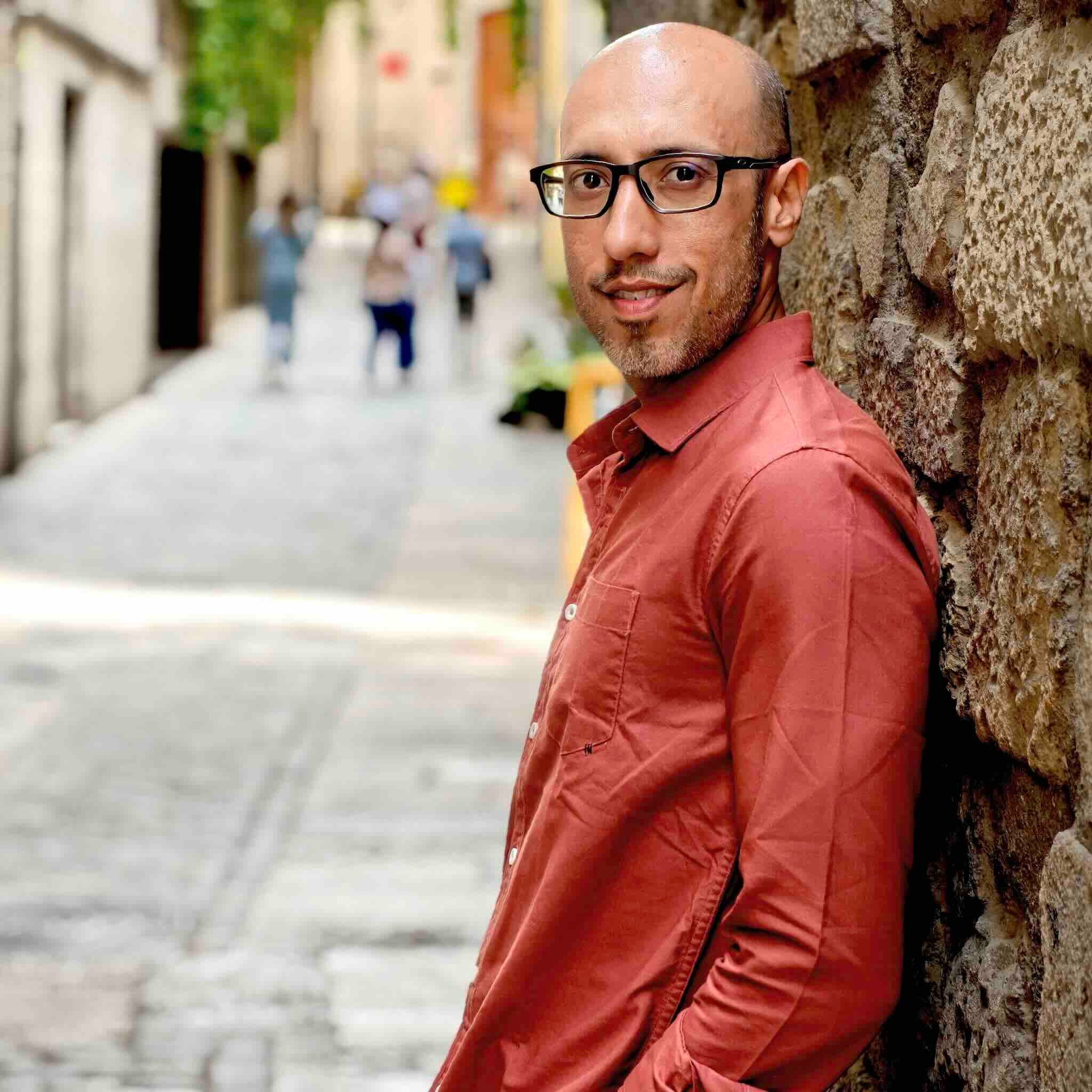 Man in a red shirt leaning against a stone wall on a street