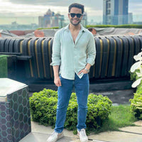 Man in light green shirt and jeans standing on a rooftop with cityscape background