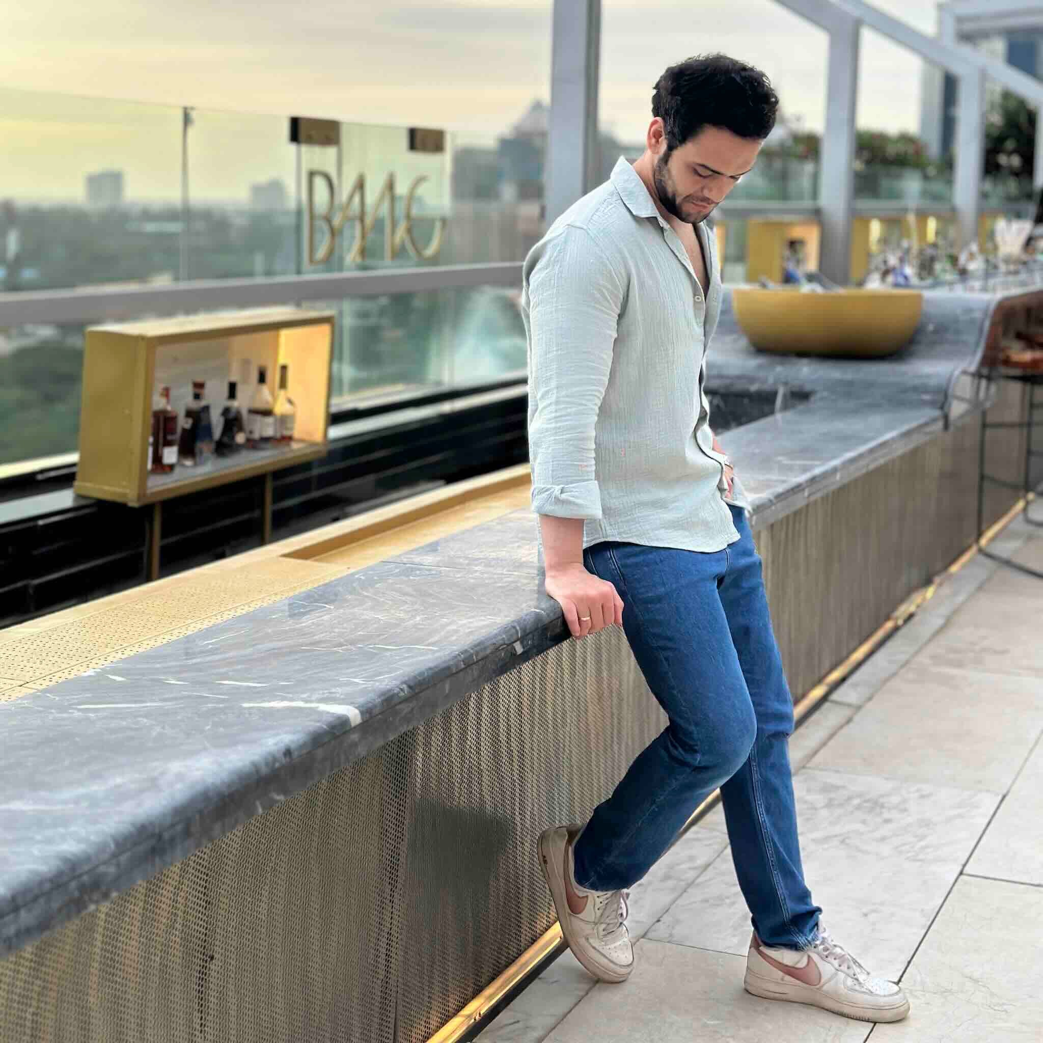 Man wearing light green shirt leaning on a railing with a cityscape background