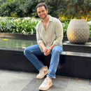 Man wearing light green shirt sitting outdoors by a pool with greenery in the background