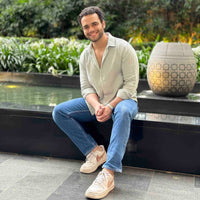 Man wearing light green shirt sitting outdoors by a pool with greenery in the background