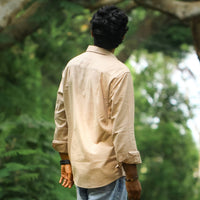 Person wearing a beige shirt and blue jeans standing in a forest