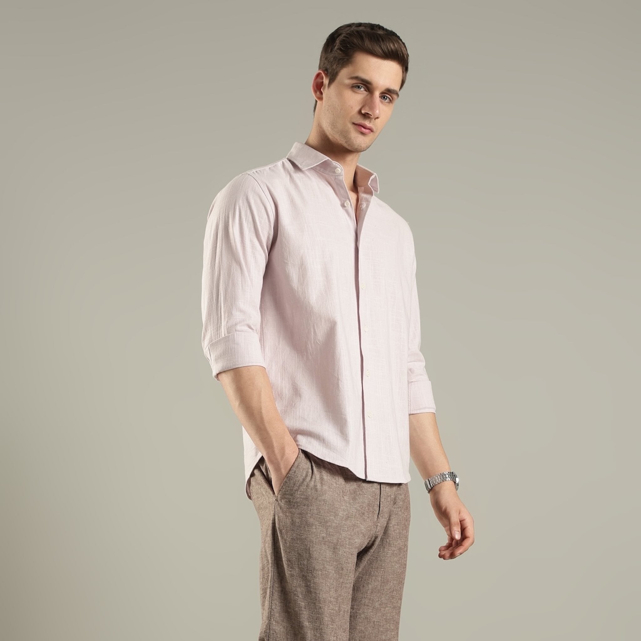Man wearing a light pink shirt hemp  and brown pants against a plain background