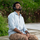 Man wearing light blue shirt and is wearing headphones sitting outdoors with a blurred natural background