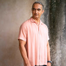 Man wearing a light pink shirt standing against a textured wall.